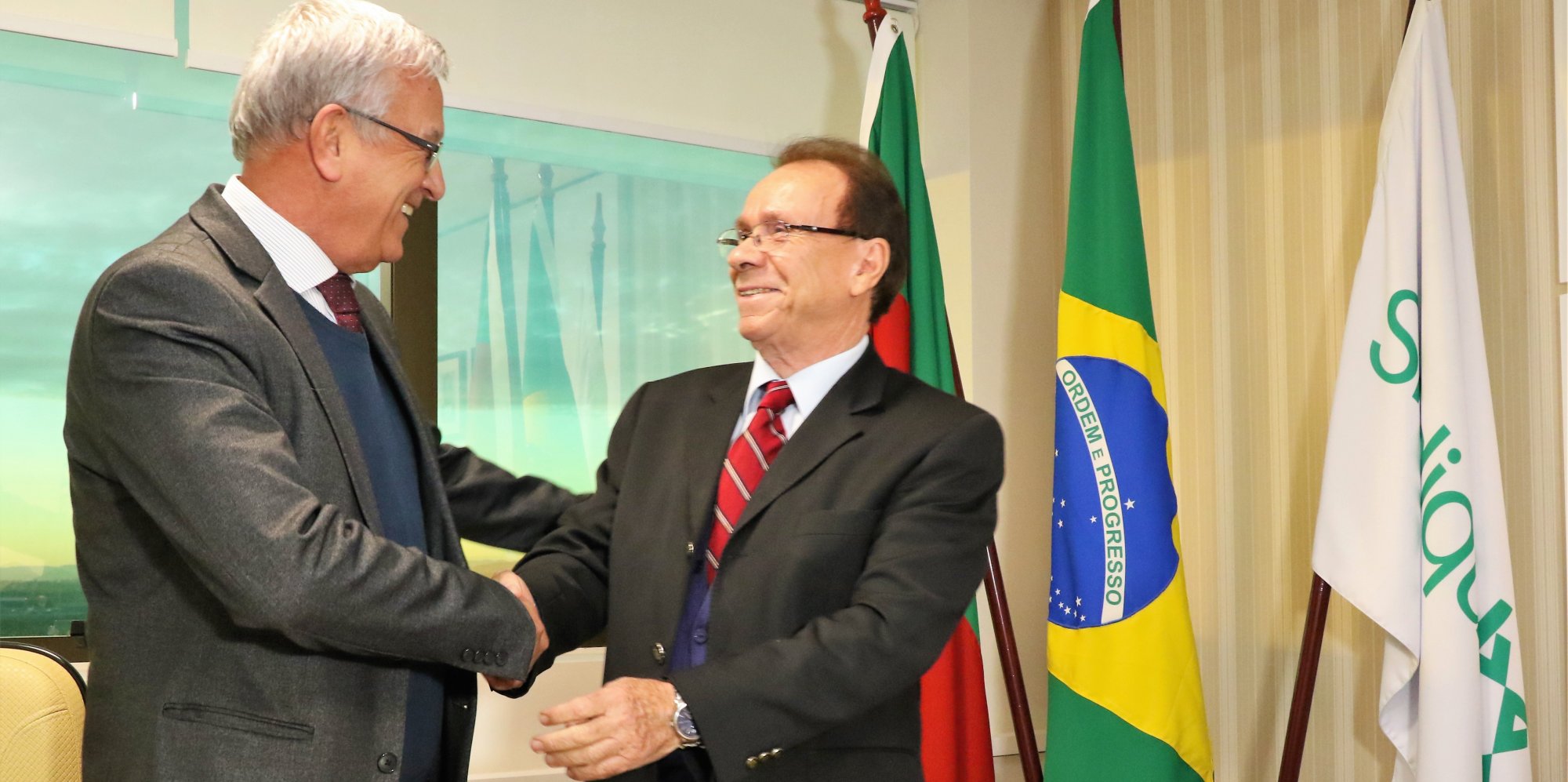 Posse Sindiquim 2019 Dois homens dando um aperto de mãos em comemoração. Três bandeiras ao lado direito