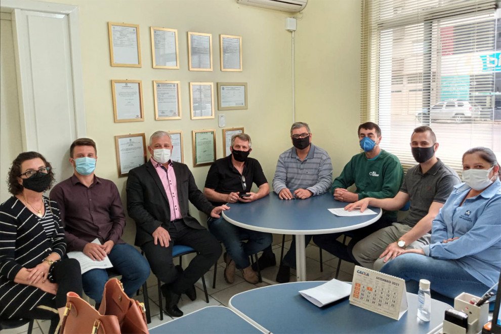 Pessoas de máscaras sentadas ao redor de mesas com cadeiras em uma sala